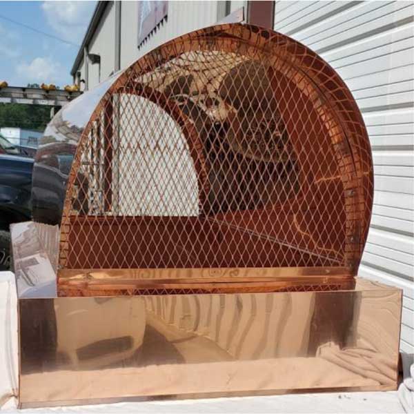 Original photo of Custom Copper Outside Mount Traditional Hood-Owens Chimney Covers Custom copper chimney cap sitting on table in front of garage door out warehouse