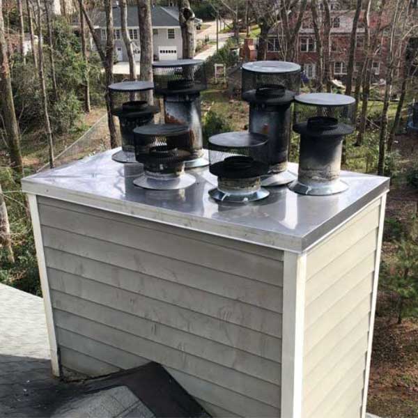 Original photo of Stainless Steel Multi Flue Chase Cover-Owens Chimney Covers Multi flue chase covers with two homes in background with trees