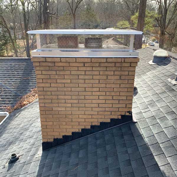 Original photo of Stainless Steel Outside Mount Flat Lid-Owens Chimney Covers Stainless Steel Outside Mount Flat Lid with black roofing and trees in background