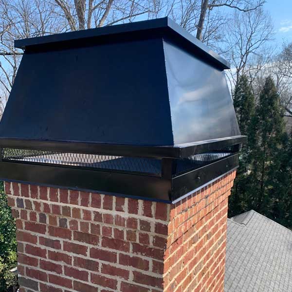Original photo of stainless steel shroud-Owens Chimney Cover Stainless steel black shroud on red brick chimney with trees in background